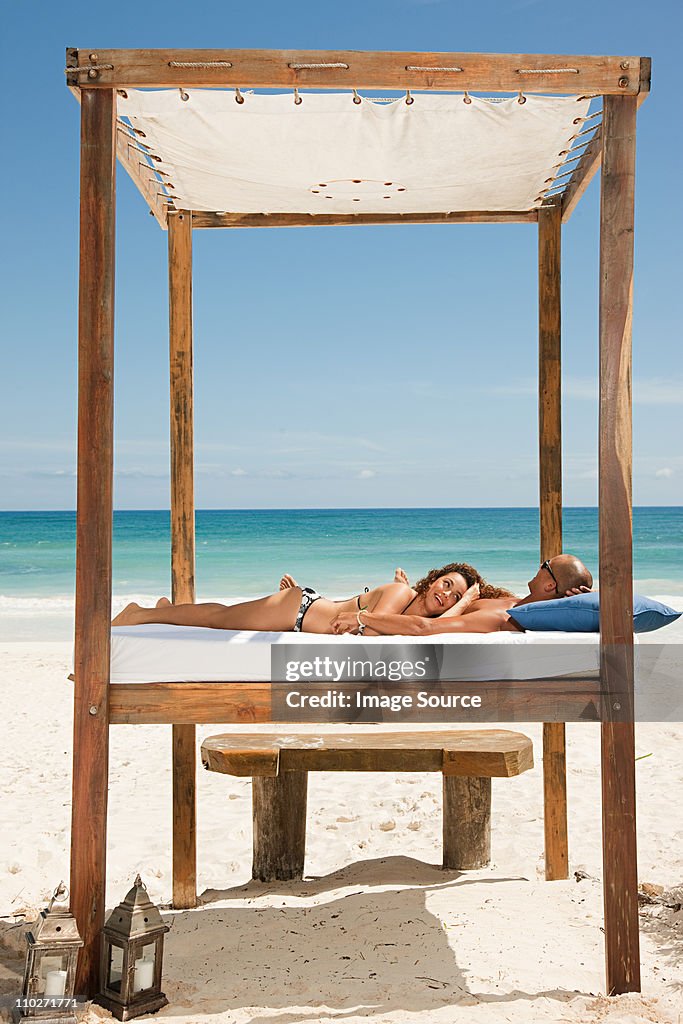 Couple on bed on sandy beach on vacation