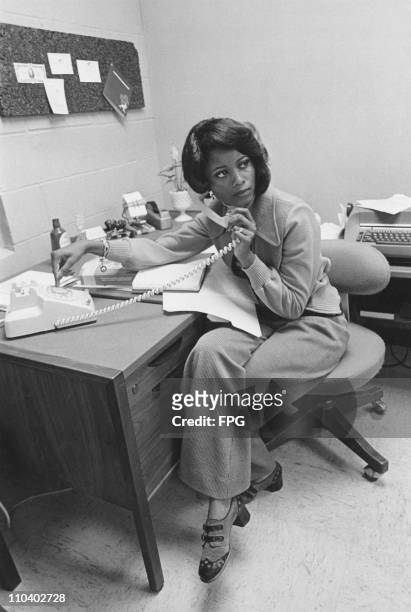 An African-American office worker takes a phone call, USA, circa 1975.