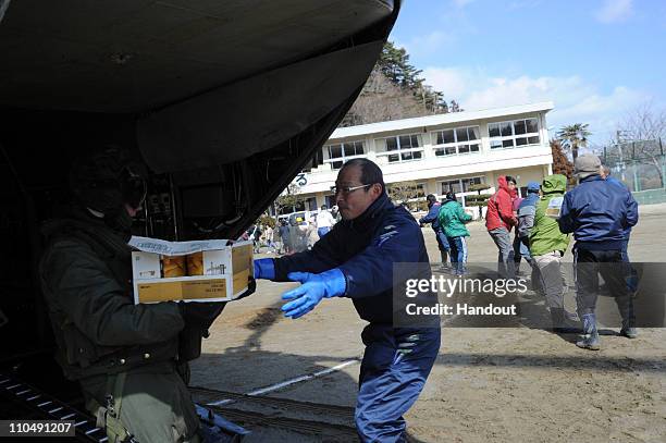 In this handout image provided by the U.S. Navy, Sgt. James Ryan from Marine Medium Helicopter Squadron 265 passes a box of food to a volunteer March...