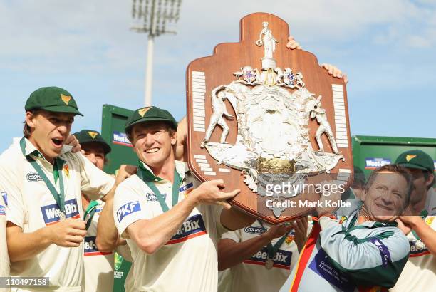 George Bailey of the Tigers and Tigers head coach Tim Coyle lift the Shield Shield after winning on day five of the Sheffield Shield final match...
