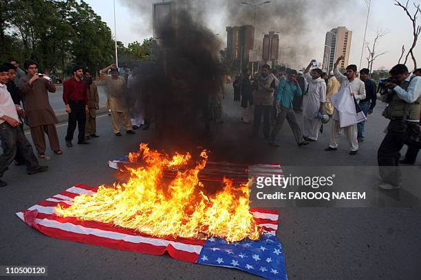 Pakistani Shiite students gather around burning US flags during a protest in Islamabad on March 20 against the killings of civilians during Libya and...