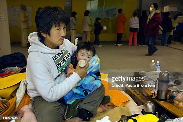 Father feeds his baby as displaced earthquake victims line up for a meal as hundreds pack a evacuation center on March 22, 2011 in Kesennuma, Miyagi,...