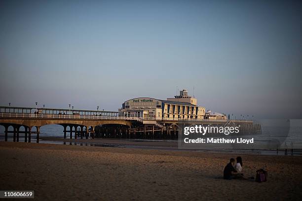 Couple sit on the beach in front of Bournemouth Pier at sunset on March 21, 2011 in Bournemouth, England. Located on the South Coast, the traditional...