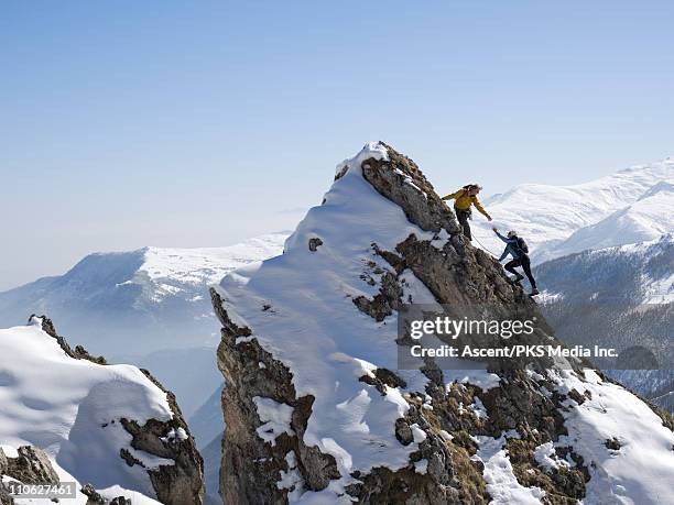 climber helps teammate to summit of pinnacle - climbing snow mountain stock pictures, royalty-free photos & images