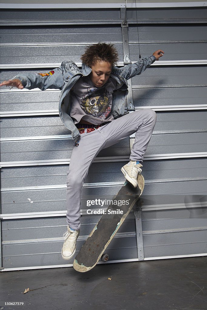 Teen boy jumping on skateboard in garage