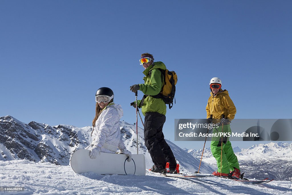Teenage snowboarders/skiers pause on ridge crest