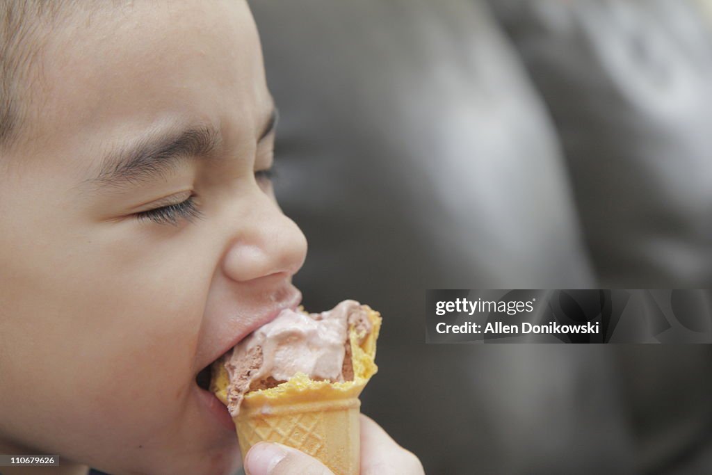 Boy closing eyes and biting ice cream cone