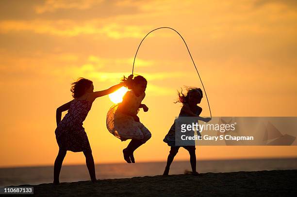 three sisters play jumprope on beach in hawaii - children playing silhouette stock pictures, royalty-free photos & images