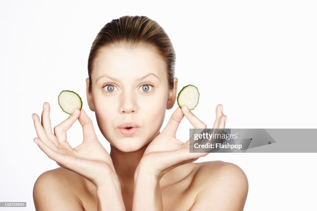 Woman holding two slices of cucumber