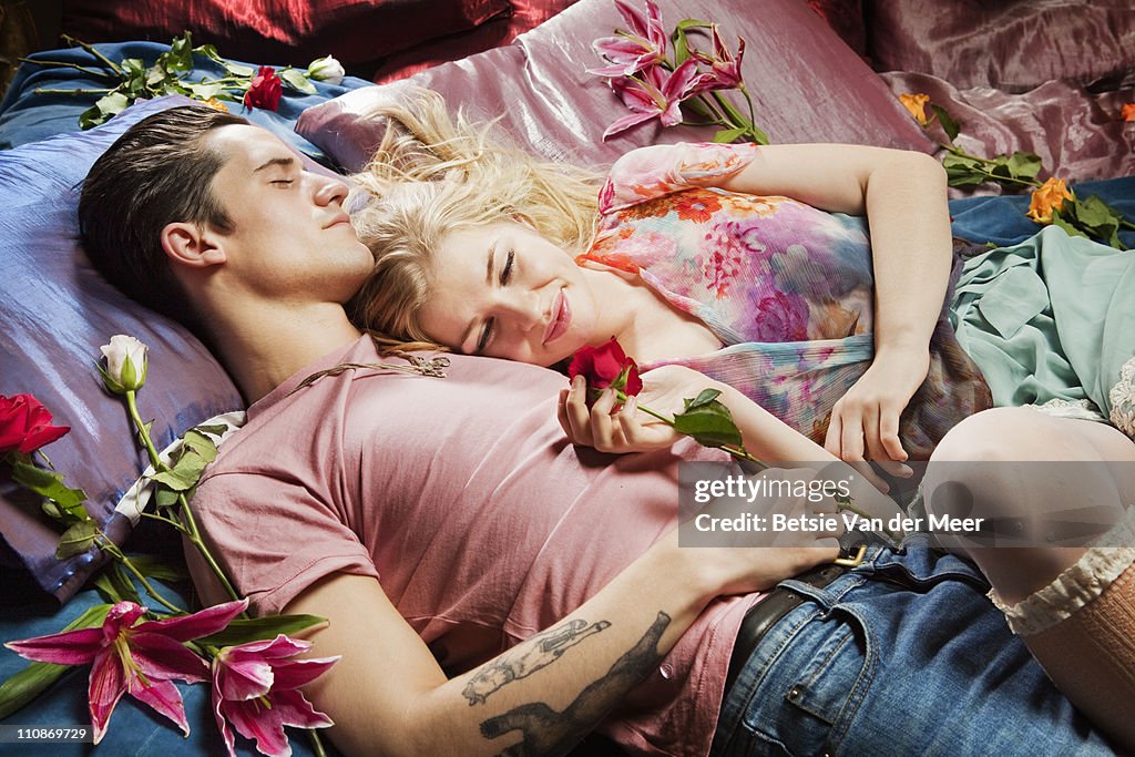 Couple laying on bed surrounded by flowers.