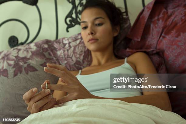 young woman lying in bed, removing her wedding ring - taking off wedding ring stock pictures, royalty-free photos & images