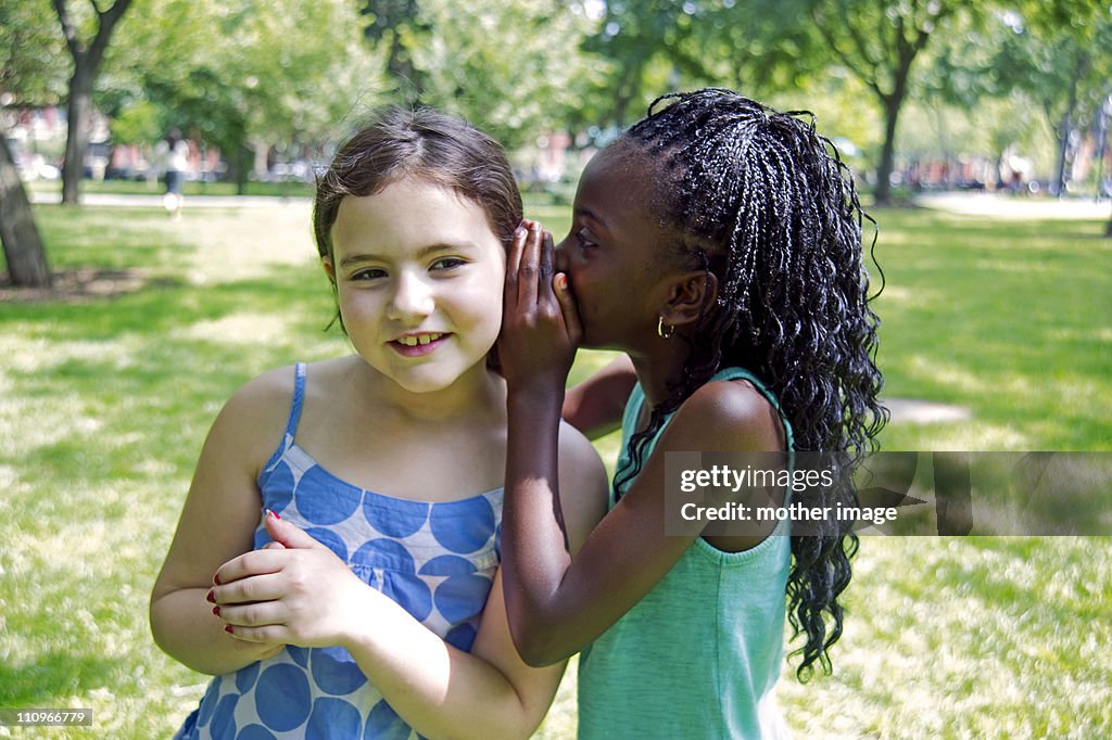 Best Friends in park whispering to each other