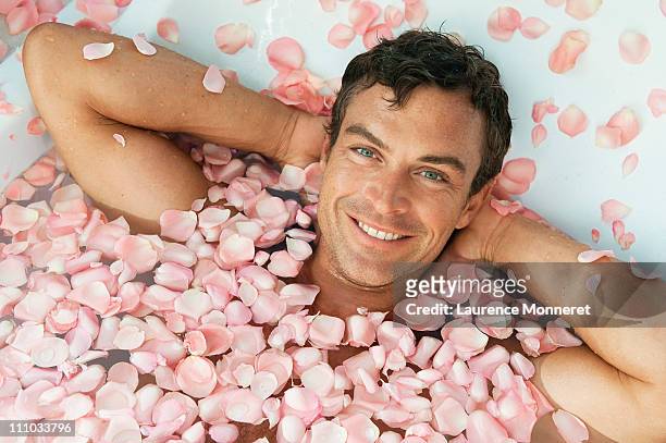 smiling man relaxing in bath with roses petals - perfektion stock-fotos und bilder