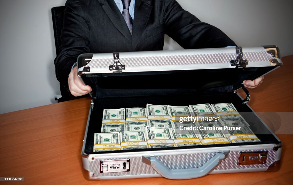 Man holding silver briefcase full of $100 bills