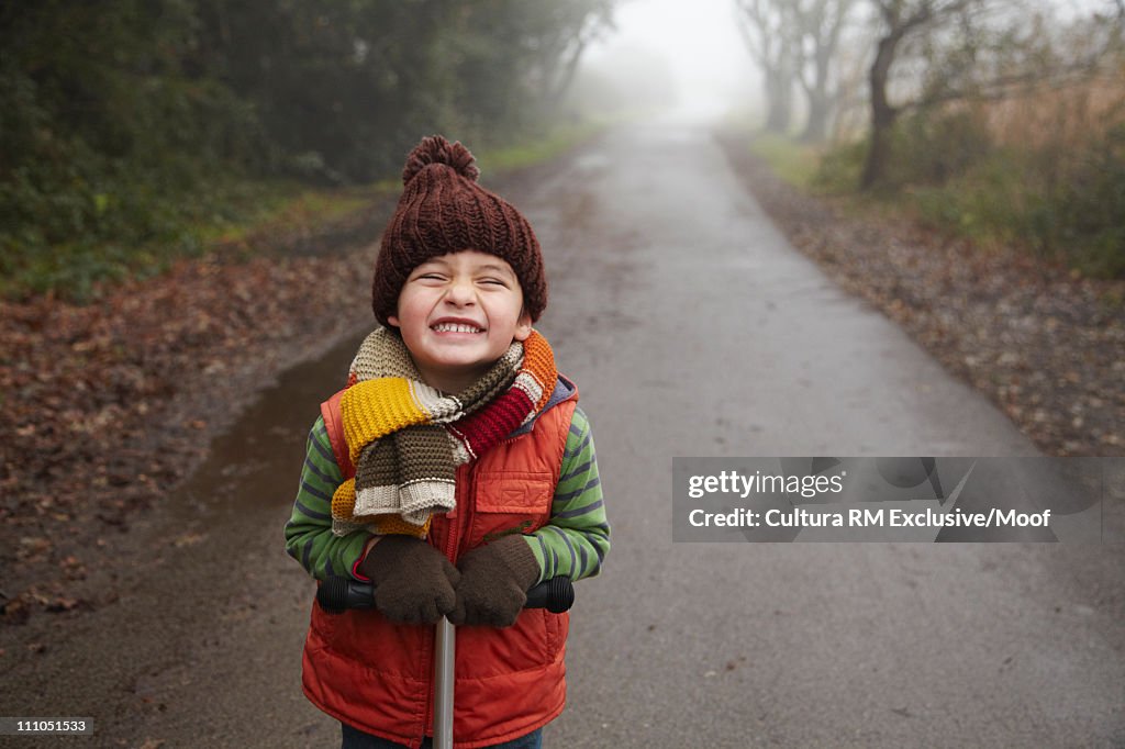 Boy in warm clothes on wet path grinning