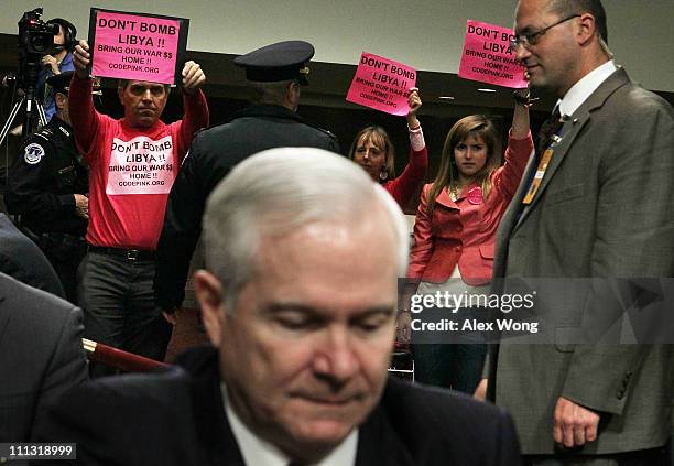 Members of Code Pink, Tighe Barry, Medea Benjamin, and Alli McCracken, hold signs as U.S. Secretary of Defense Robert Gates takes his seat during a...