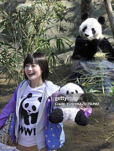 Girl smiles as she holds a panda doll before the giant female panda Shin Shin eating bamboo at Tokyo's Ueno Zoo on April 1, 2011. A pair of pandas,...