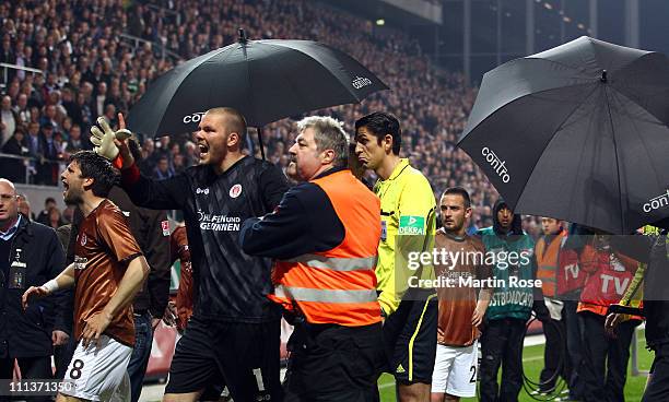 Referee Deniz Aytekin is protected by umbrellas after the Bundesliga match between FC St. Pauli and FC Schalke 04 at Millerntor Stadium on April 01,...