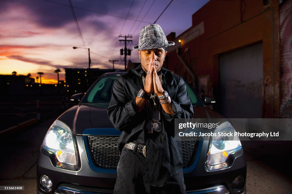 Hip African American man praying near car at night