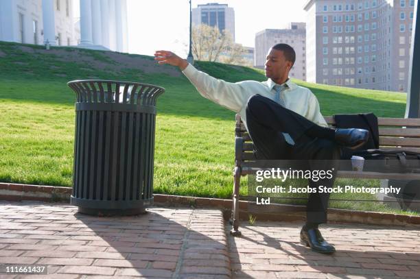 african american businessman throwing trash in garbage can - garbage man stockfoto's en -beelden