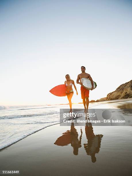 couple walking on beach carrying surfboards - newport beach california stockfoto's en -beelden