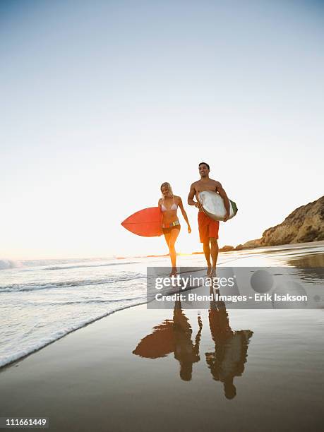 couple walking on beach carrying surfboards - newport beach california stock pictures, royalty-free photos & images