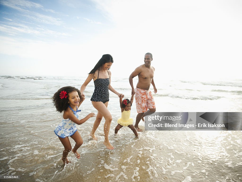 Family holding hands and wading through ocean water