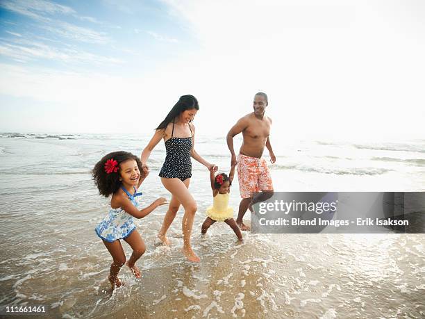 family holding hands and wading through ocean water - beach family stockfoto's en -beelden