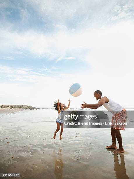 black father throwing ball on beach with daughter - enfants plage photos et images de collection