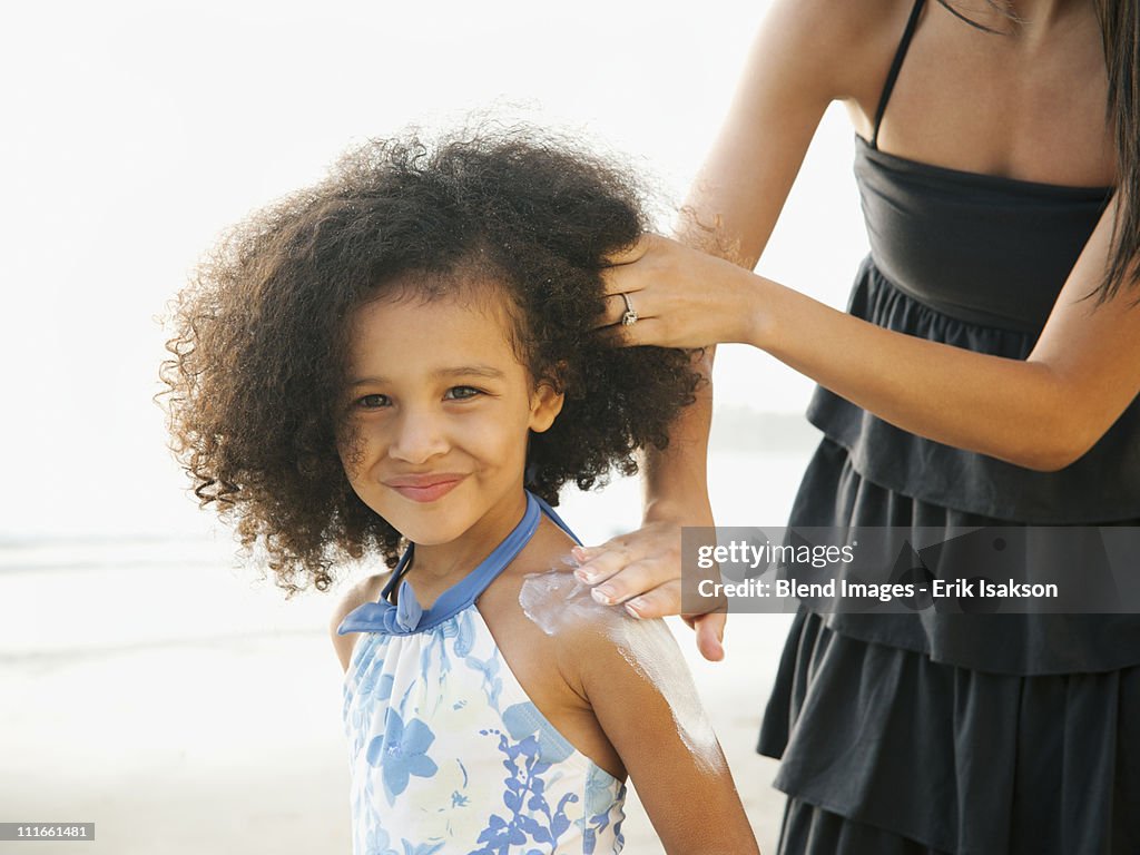 Hispanic mother rubbing sunscreen on daughter at beach