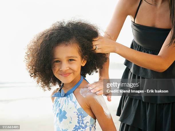 hispanic mother rubbing sunscreen on daughter at beach - applying sunscreen stock pictures, royalty-free photos & images