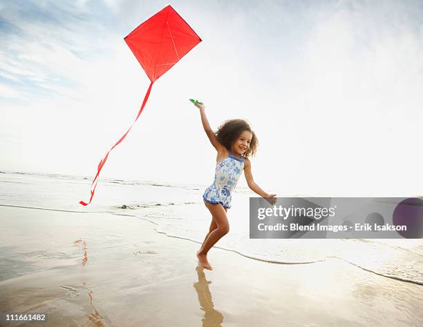 mixed race girl running with kite on beach - kite flying photos et images de collection