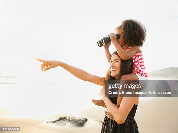 hispanic mother carrying daughter with binoculars on beach - child with binoculas stockfoto's en -beelden