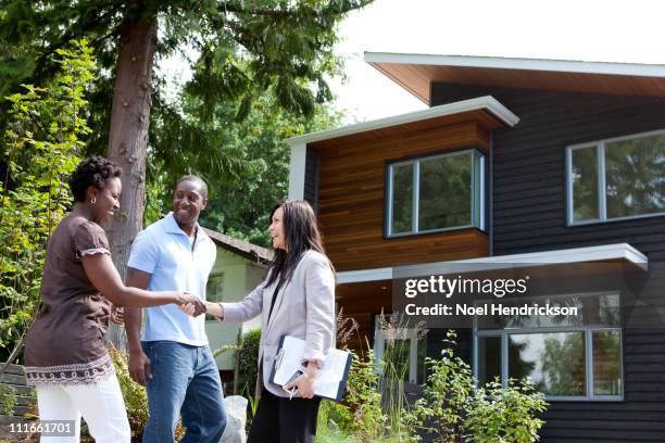 real estate agent greeting couple at house - estrenar casa fotografías e imágenes de stock