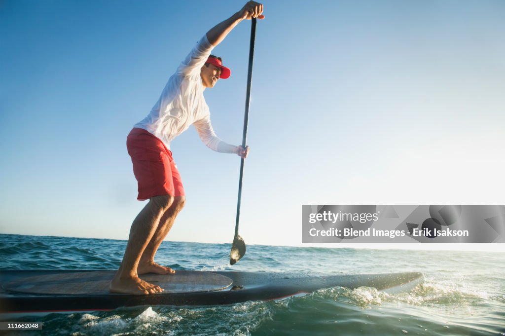 Mixed race man paddling on surfboard