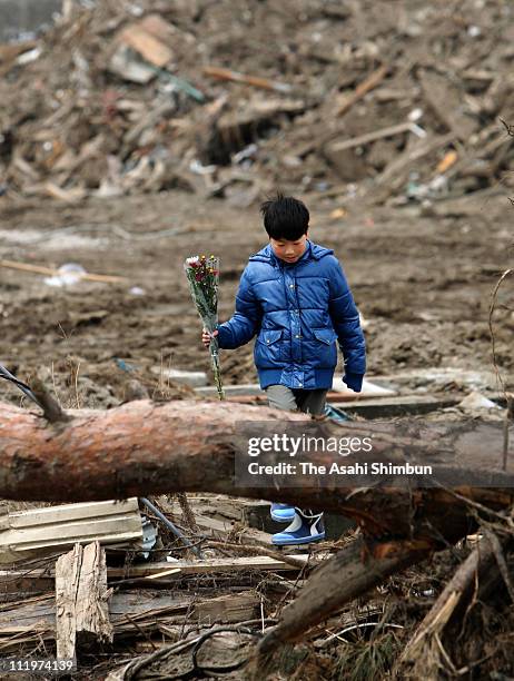 Boy who lost friends during the tsunami holds a bunch of flowers as he walks near Okawa Elementary School on April 11, 2011 in Ishinomaki, Miyagi,...