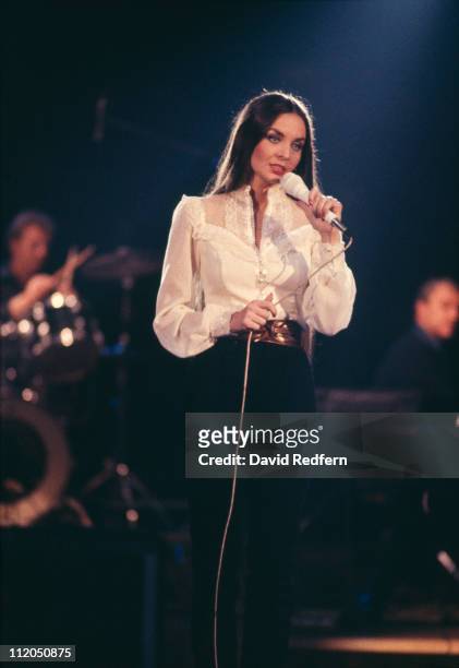 Crystal Gayle, U.S. Country music singer, singing into a microphone during a concert, circa 1975.