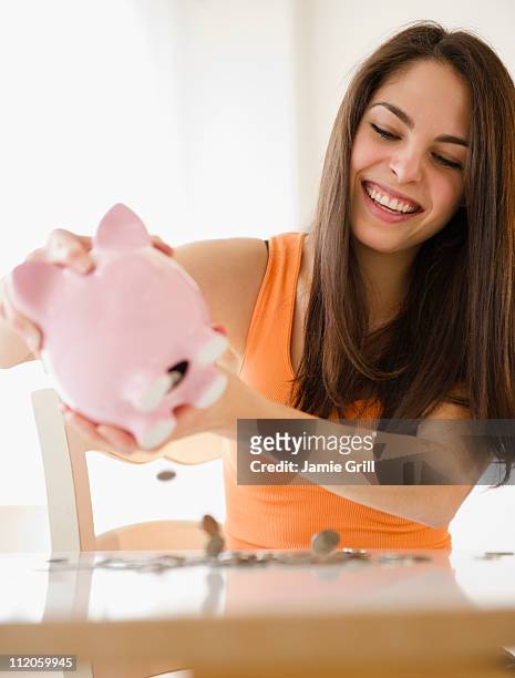 young woman emptying piggy bank, smiling - happy piggy bank stock pictures, royalty-free photos & images