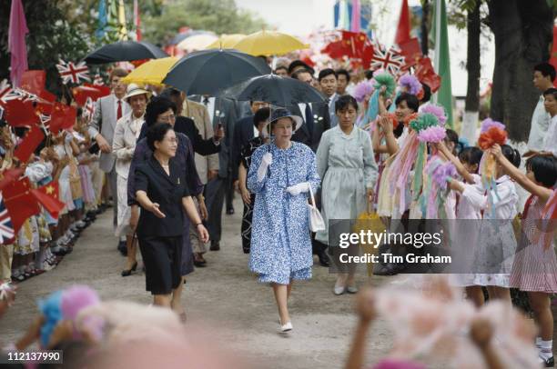 Queen Elizabeth II, sheltered by an umbrella, meets children at the Children's Palace in Canton, during an official State Visit to China, 18 October...