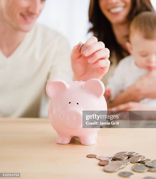 family adding coins to piggy bank together - couple saving piggy bank ストックフォトと画像