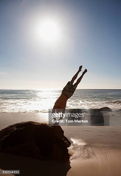 man doing handstand on rock at beach - handstand beach stock pictures, royalty-free photos & images