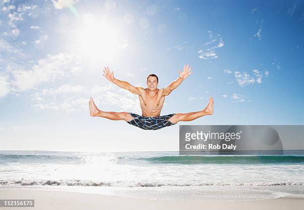 mann, springen in der luft am strand - mann freudensprung sonne vorderansicht leger stock-fotos und bilder