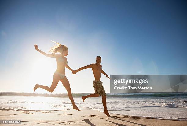 coppia mano nella mano e in esecuzione sulla spiaggia - couple running on beach foto e immagini stock