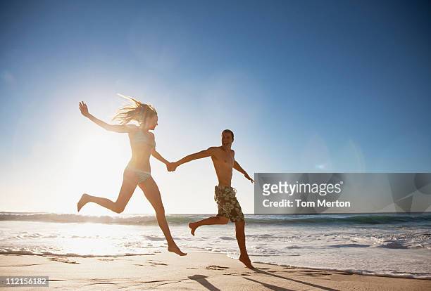 couple holding hands and running on beach - couple running on beach stock pictures, royalty-free photos & images