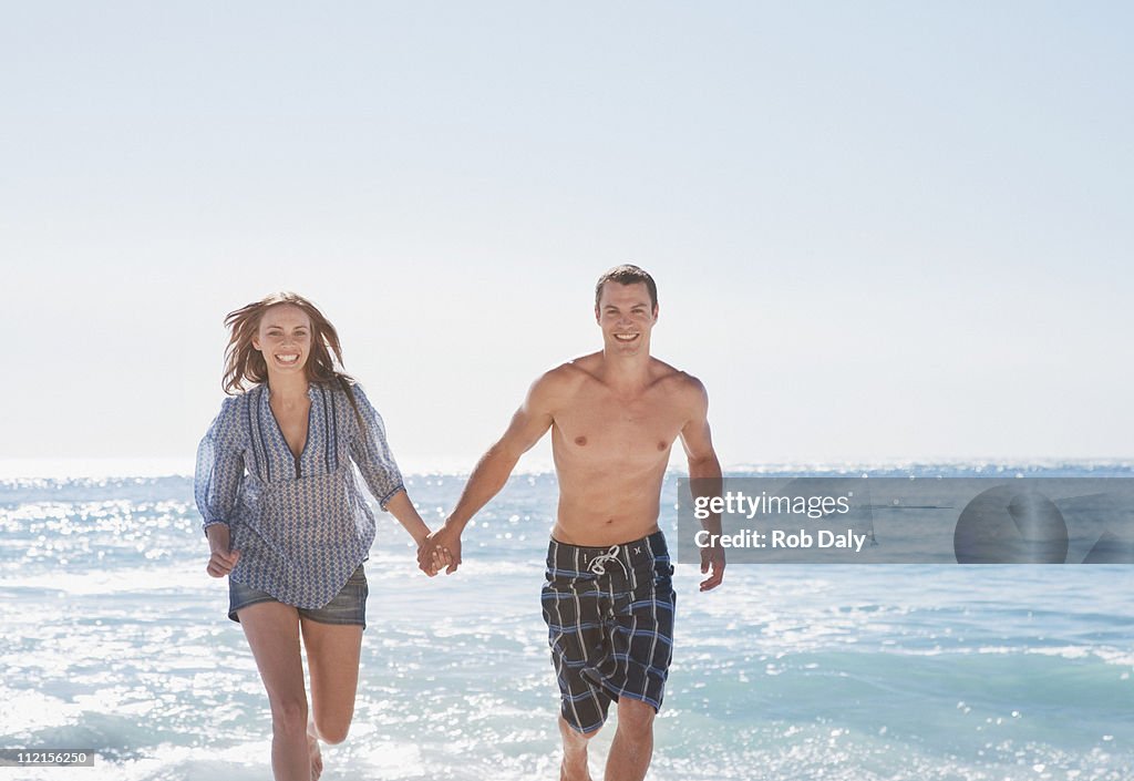Smiling couple running on beach and holding hands