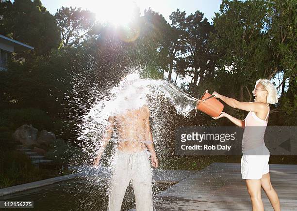 playful woman throwing bucket of water on boyfriend - gooien stockfoto's en -beelden