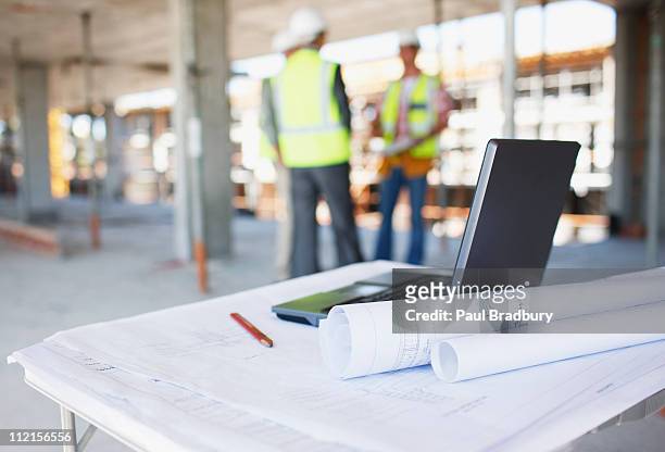 trabajadores de la construcción detrás blueprints y computadora portátil en constructio - plano documento fotografías e imágenes de stock