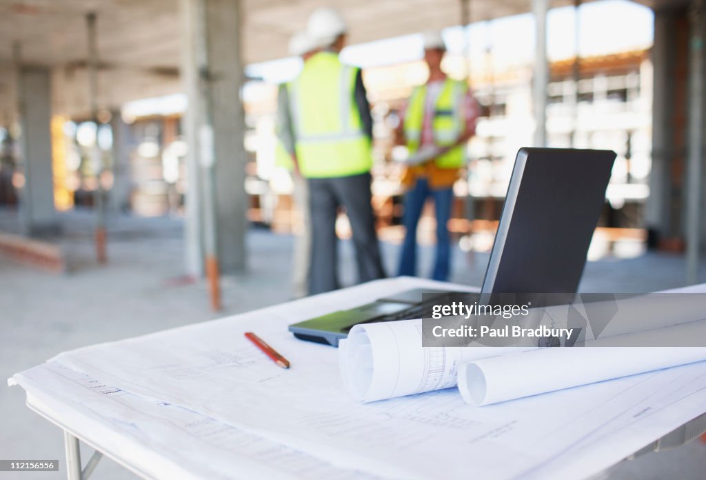 Construction workers behind blueprints and laptop on construction site