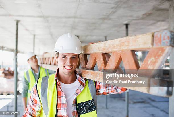 bau arbeiter tragen tragender balken auf baustelle - construction worker stock-fotos und bilder