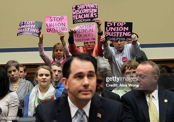 Members of Code Pink Medea Benjamin, Liz Hourican and Tighe Barry, hold signs to protest as Wisconsin Gov. Scott Walker takes his seat during a...